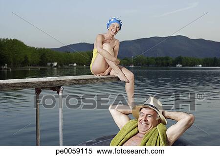 Stock Image - Woman sitting on wooden plank over lake with man in inner tube floating by. Fotosearch - Search Stock Photos, Mural Pictures, Photographs, and Photo Clipart