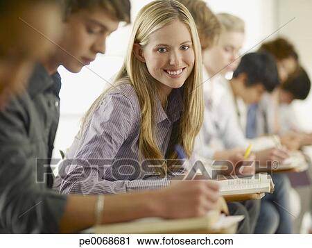 Smiling College Student Sitting At Desk In Classroom Stock Image