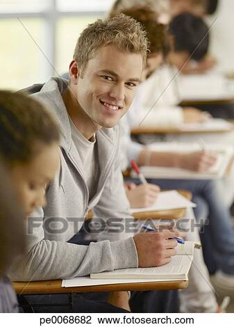 Smiling College Student Sitting At Desk In Classroom Stock Image