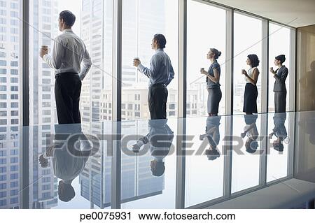 Business People Drinking Coffee And Looking Out Window In Conference Room Stock Image