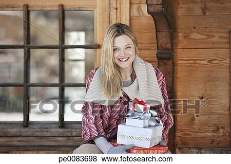 Portrait Of Smiling Woman Holding Christmas Gifts On Cabin Porch