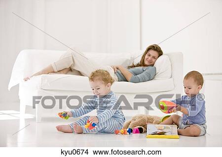 Picture - Babies playing with toys and their mother resting on a couch. Fotosearch