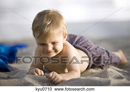 Stock Image - Baby boy lying on sand. Fotosearch