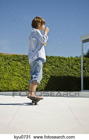 Stock Image - Boy blowing bubbles with a bubble wand while skateboarding. Fotosearch