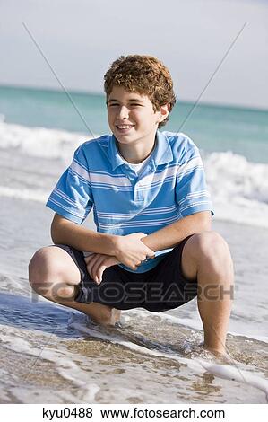 Stock Photo - Boy crouching on the beach. Fotosearch