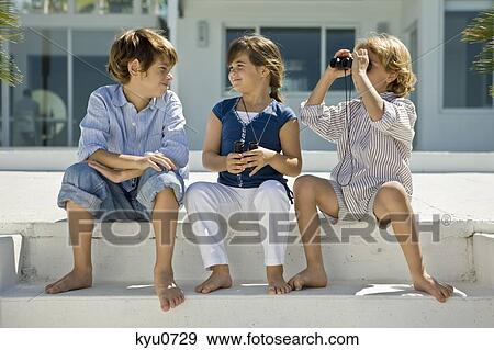 Stock Photo - Boy looking through binoculars with his friends sitting beside him. Fotosearch