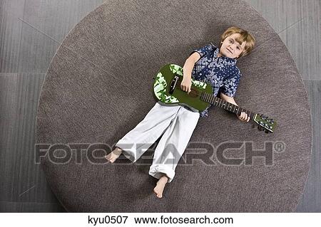 Boy lying on a round sofa and playing a guitar View Large Photo Image Stock Photo - Boy lying on a round sofa and playing a guitar. Fotosearch