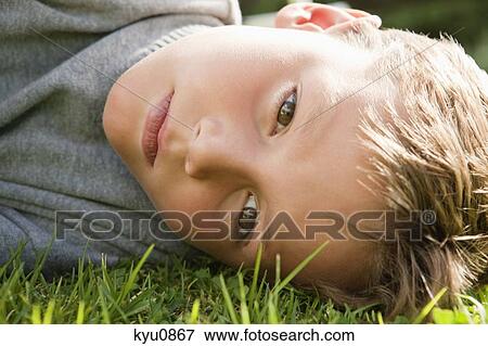 Boy lying on grass and looking serious View Large Photo Image Stock Photo - Boy lying on grass and looking serious. Fotosearch