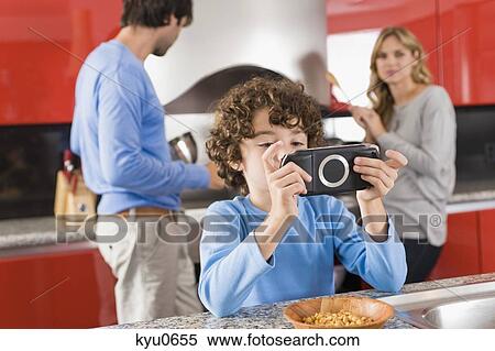 Boy playing a video game and his parents standing in the background View Large Photo Image Stock Photography - Boy playing a video game and his parents standing in the background. Fotosearch