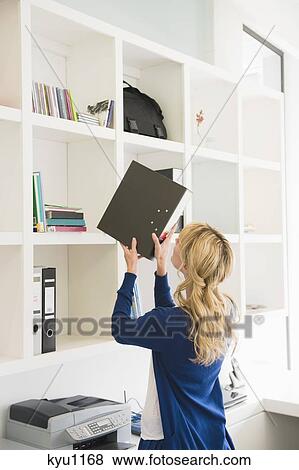 Businesswoman putting a ring binder in a shelf View Large Photo Image Stock Photo - Businesswoman putting a ring binder in a shelf. Fotosearch
