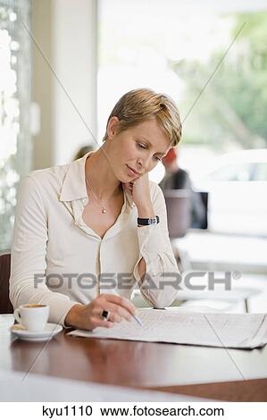 Stock Image - Businesswoman sitting in a restaurant and reading a financial newspaper. Fotosearch