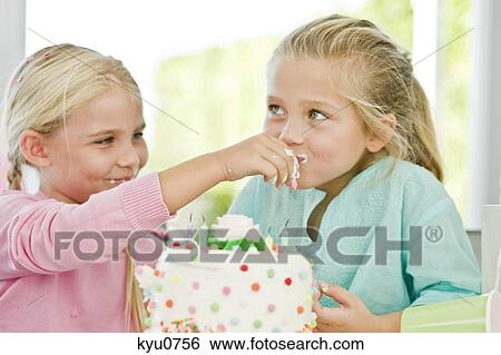 Stock Photograph - Close-up of a girl feeding a birthday cake to her sister. Fotosearch
