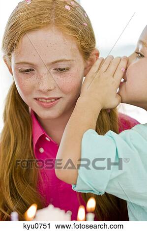 Stock Image - Close-up of a girl whispering to her sister. Fotosearch
