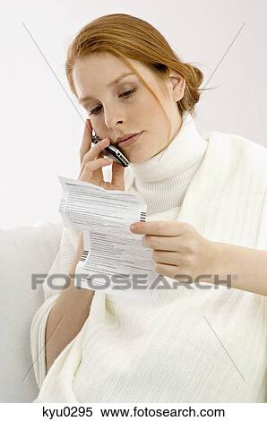 Stock Photography - Close-up of a pregnant young woman reading a medical report and talking on a mobile phone. Fotosearch