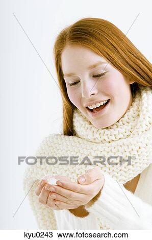Stock Image - Close-up of a young woman holding snow in cupped hands and smiling. Fotosearch