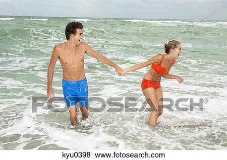 Stock Photo - Couple holding hands and walking in water on the beach. Fotosearch