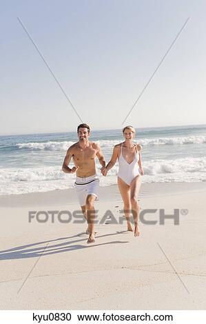 Stock Image - Couple running on the beach. Fotosearch