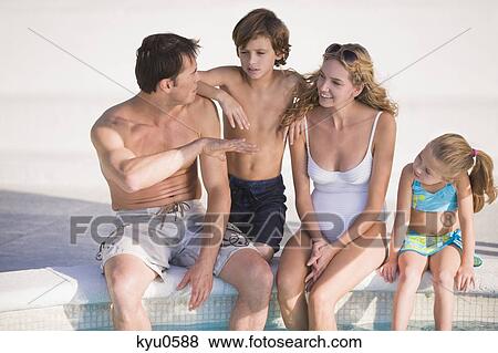 Stock Photo - Family sitting at the poolside and smiling. Fotosearch
