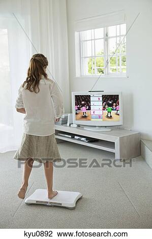 Stock Image - Girl doing step aerobics and watching TV. Fotosearch