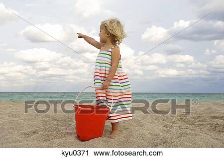 Girl holding a sand pail on the beach and pointing towards the sea View Large Photo Image Stock Image - Girl holding a sand pail on the beach and pointing towards the sea. Fotosearch