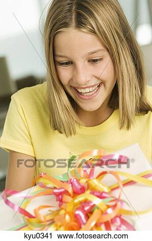 Stock Image - Girl looking at a birthday present and smiling. Fotosearch