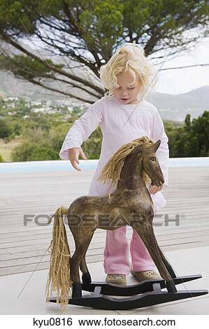 Girl standing near a rocking horse View Large Photo Image Stock Photograph - Girl standing near a rocking horse. Fotosearch