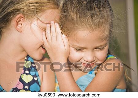 Stock Image - Girl whispering into her friend's ear. Fotosearch