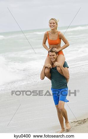 Stock Image - Man carrying a woman on his shoulders on the beach. Fotosearch