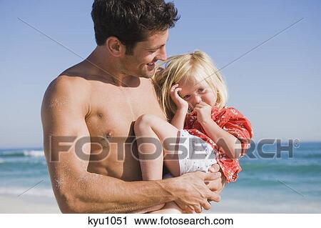 Stock Image - Man carrying his daughter on the beach. Fotosearch