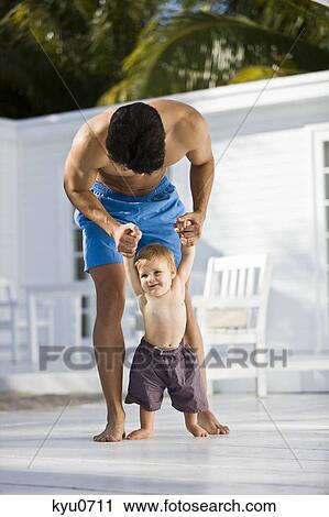 Stock Image - Man helping his son to walk. Fotosearch