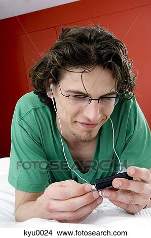 Man listening to MP3 player, lying on a bed View Large Photo Image Picture - Man listening to MP3 player, lying on a bed. Fotosearch