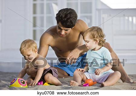 Stock Photo - Man playing with his son and daughter in sand. Fotosearch
