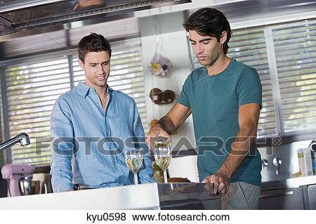 Stock Photo - Man pouring wine in glasses for his friend in the kitchen. Fotosearch