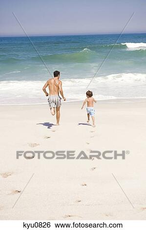 Stock Photograph - Man running with his son on the beach. Fotosearch