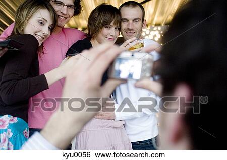 Stock Photograph - Man taking picture of 2 smiling couples. Fotosearch