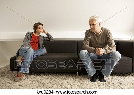 Picture - Mature man and his son sitting on a couch. Fotosearch
