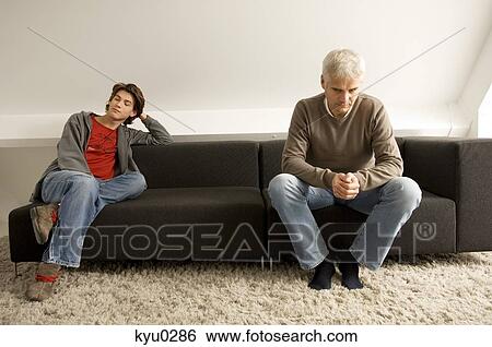 Stock Photograph - Mature man and his son sitting on a couch. Fotosearch