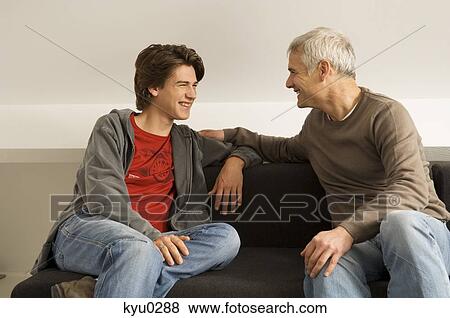 Stock Photo - Mature man with his son sitting on a couch and gossiping. Fotosearch