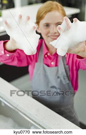 Stock Image - Portrait of a girl showing her hands covered in soap suds. Fotosearch