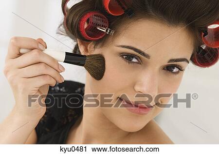 Stock Image - Portrait of a woman applying blusher on her face. Fotosearch