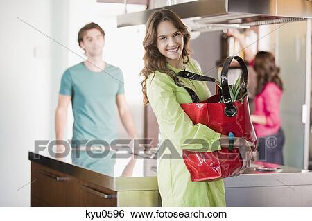 Stock Photograph - Portrait of a woman holding a shopping bag in the kitchen. Fotosearch