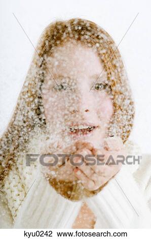 Stock Image - Portrait of a young woman blowing snow from her cupped hands. Fotosearch