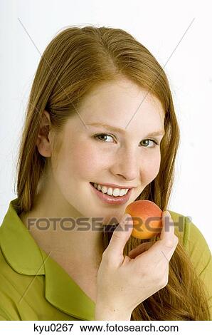 Portrait of a young woman eating an apricot and smiling View Large Photo Image Stock Photo - Portrait of a young woman eating an apricot and smiling. Fotosearch