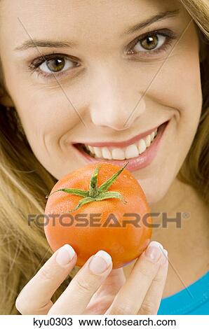 Portrait of a young woman holding a tomato and smiling View Large Photo Image Stock Image - Portrait of a young woman holding a tomato and smiling. Fotosearch