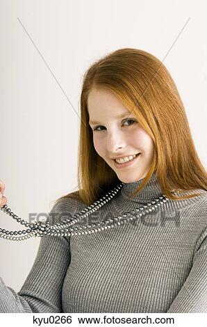 Portrait of a young woman holding her necklace and smiling View Large Photo Image Stock Photograph - Portrait of a young woman holding her necklace and smiling. Fotosearch