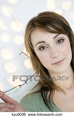 Portrait of a young woman holding pair of glasses View Large Photo Image Stock Photograph - Portrait of a young woman holding pair of glasses. Fotosearch