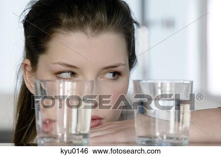 Portrait of a young woman looking at 2 glasses of water View Large Photo Image Stock Photograph - Portrait of a young woman looking at 2 glasses of water. Fotosearch