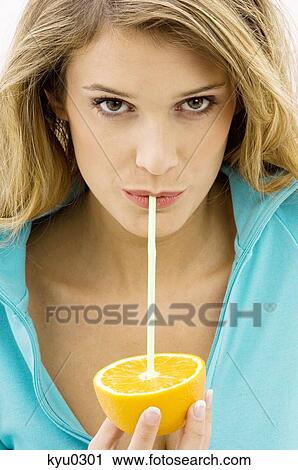 Stock Image - Portrait of a young woman sipping from an orange with a drinking straw. Fotosearch
