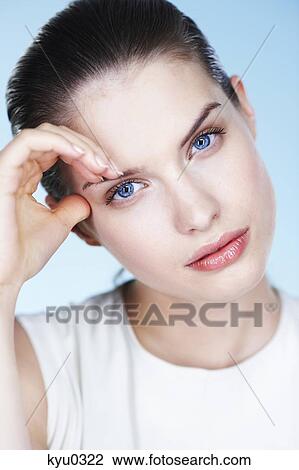 Stock Image - Portrait of young woman, hand on forehead. Fotosearch