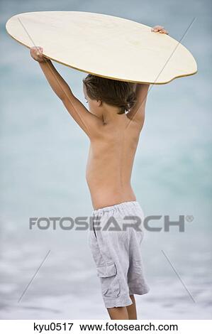 Rear view of a boy holding a body board over his head View Large Photo Image Stock Photo - Rear view of a boy holding a body board over his head. Fotosearch